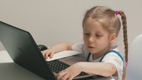 closeup slow motion little girl student sits at table with notebook laptop, blonde with pigtails child bored reasoning, presses buttons on keyboard