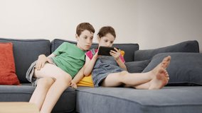 Two kids sitting on a large sofa at home, using a mobile phone