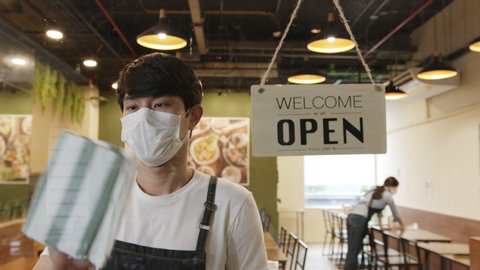 Business reopen again concept asian man working in a restaurant turning open sign at front to open after lockdown and epidemic of coronavirus covid-19