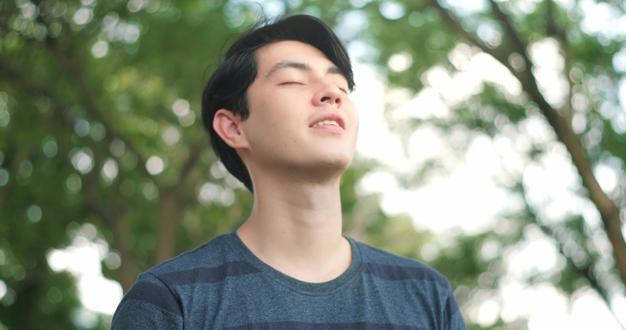 Handsome man taking deep breath, Young man relaxing breathing in fresh crisp air in green background. Stop and smell the tree, connect with nature. | Shutterstock HD Video #1055198636