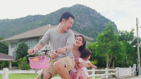 Asian family ride a bicycle and having fun together. Father bike, mother holding baby child on back seat talking and laughing. Parents and daughter activity, kid feeling happy with big smile on face.