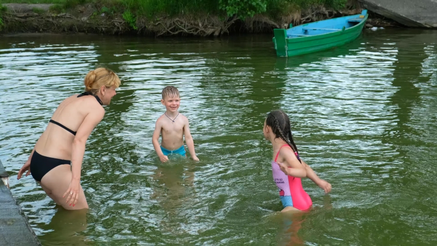 Mother son and daughter splashing water on the lake. Slow motion. Family vacation in nature in summer.