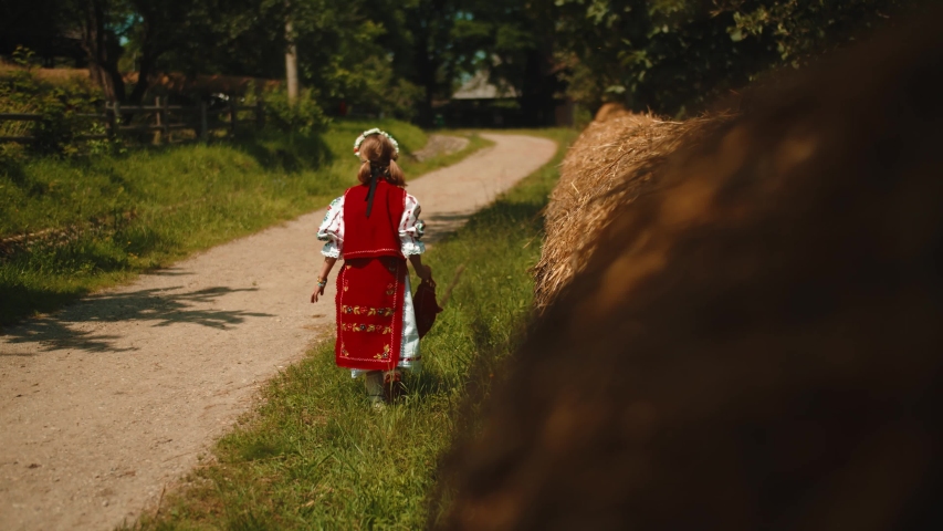 Little girl dressed in traditional costume walking down a countryside road. Village life in Eastern Europe, Romania