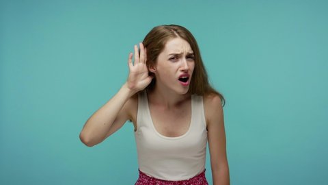 What? I can't hear you! Confused girl having hearing problems, asking to say louder, difficult to listen quiet talk, misunderstanding in communication. indoor studio shot isolated on blue background