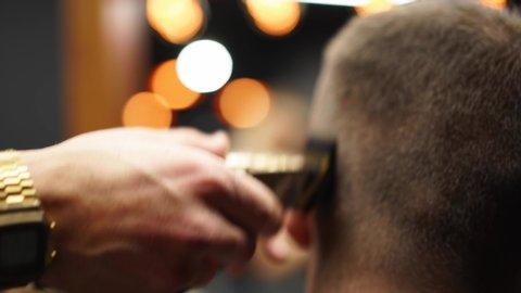 Trendy barber cuts bearded man's hair with a clipper in barbershop. Men's hairstyling and hair cutting in salon. Grooming the hair with trimmer. Hairdresser doing haircut in retro hair salon.
