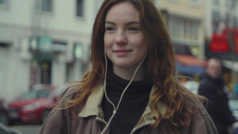 Young caucasian woman standing on city street listening to audiobook on earphones. Close up.