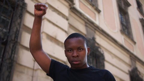 A young African American man protests against police violence and racism. Close portrait of a black man with his fist raised up. Black lives matter