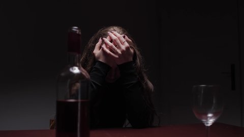 Young beautiful woman in severe depression, drinking alcohol. The concept of abuse and alcoholism. Alcoholic woman with bottle and glass of wine. Camera movement: Truck left