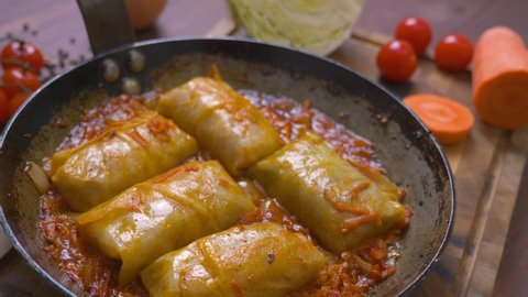 Pan with stuffed cabbage leaves on wooden brown table. Ingredients for making cabbage rolls are on the table next to the stuffed cabbage cooked in the pan.