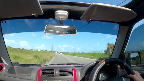 BRIDGETOWN, BARBADOS, CARIBBEAN ISLANDS, DECEMBER 2019: POV: Tourist driving his jeep on fun road trip in Barbados approaches a small village. Man drives a Suzuki SUV down a rural road near Bridgetown