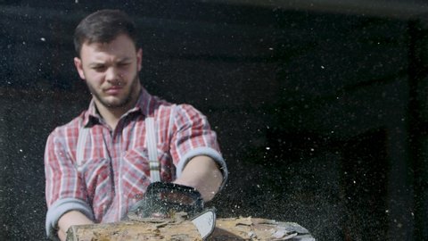 Brutal man saws log. Video. Sexy man in checked shirt saws log with powerful hand saw. Slow-motion video of sawing logs with flying sawdust