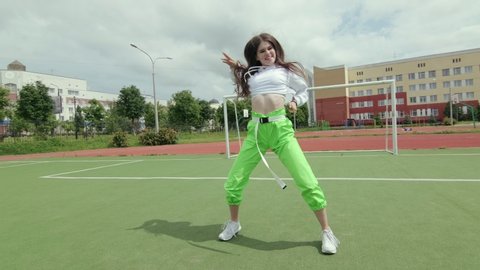 young woman with long hair in tracksuit dancing street modern dance, dancehall twerk, shaking her buttocks on a Sportsground. Urban dancing freestyle in the city. Booty Dance.  Gimbal shot