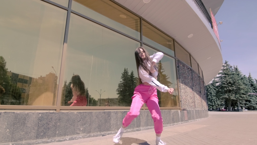 funny girl performing cool dance opposite the building with mirrored glass. Concept of learning hip hop and break dance technique. Youth subculture. Contemporary choreography. Gimbal shot. Slow motion Royalty-Free Stock Footage #1055230499