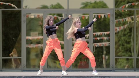 two young women with long hair in tracksuits dancing dancehall twerk, street modern dance in front of the building. Booty Dance