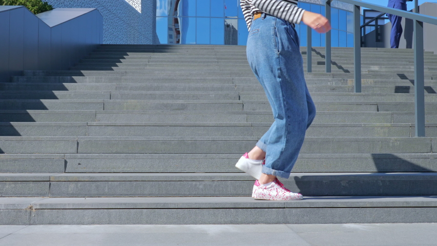 A happy teenage girl is dancing a shuffle on the stairs and enjoying life next to a modern building. The concept of carefree, youth culture and city life Royalty-Free Stock Footage #1055232974