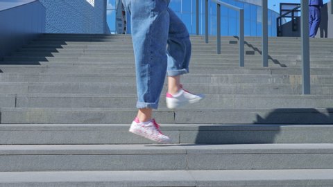 A happy teenage girl is dancing a shuffle on the stairs and enjoying life next to a modern building. The concept of carefree, youth culture and city life