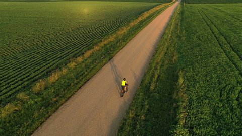 Cyclist is riding american countryside. Riding bike, touring, outdoor activities concept. Aerial view, drone following, tracking shot. Rural scenery, sunny morning, sunrise, summertime