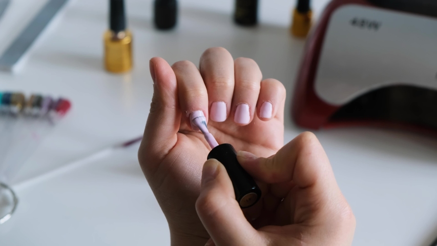 Close up of the woman's hand applying UV gel covering on her nails. the woman is covering her nails with the light nail polish UV gel. Female manicure in the light environment.Fingernail treatment Royalty-Free Stock Footage #1055235569