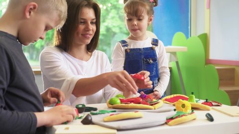 Caucasian girl and boy kid playing and learning at preschool with female teacher. Mother, daughter adn son playing cooking