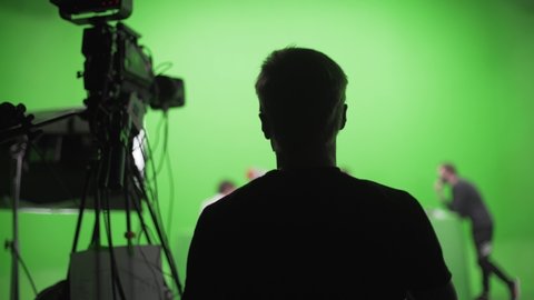 Film crew in green studio shooting video. Chroma - technology of combining two or more images or frames in single composition. Cameraman,director,crew. Filmmaking industry.