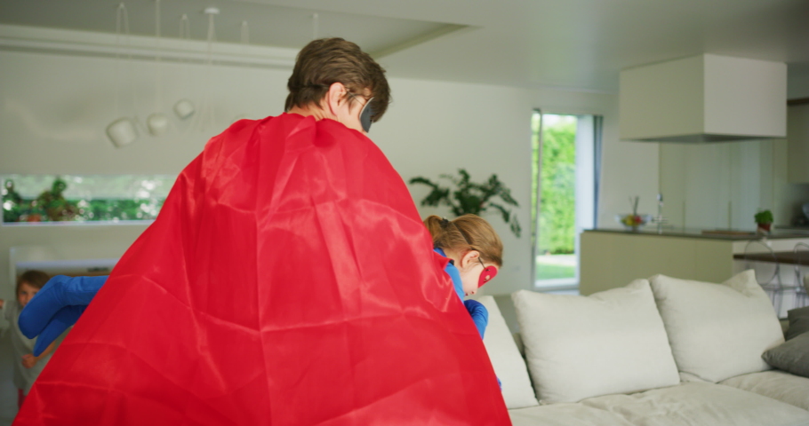 A carefree happy smiling father and daughter dressed as superheroes are having fun to run and jump while playing an imagination game at home.