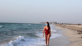 Woman walking on a beach with mask. Tourism during coronavirus. Protection during coronavirus. Travelling after coronavirus ends. Post lockdown tourism, Coronavirus safety at public places. New Rules.