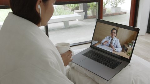 Asian woman talking with doctor via computer laptop virtual video call or video conference, telehealth and telemedicine concept
