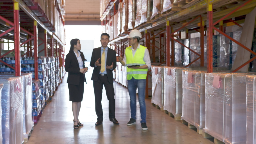 Long to medium shot : Asian engineer walking and explaining about stock in storage warehouse. Visitor or customer visiting to looking stock and plant before merge and acquisition the factory company. Royalty-Free Stock Footage #1055243360
