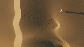 A young beautiful model in a white casual outfit is walking through the natural landscape. 4K Aerial drone footage of a woman making footprints on the sandhill at sunrise. California, USA