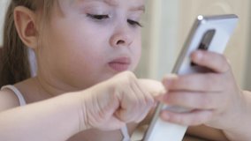 Little girl plays in a smartphone. The child learns remotely in the phone application. Preschooler on the Internet. Close-up.