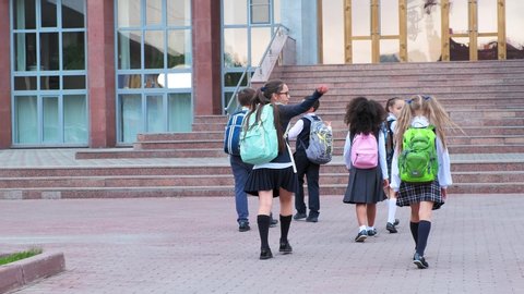 junior students in uniform with schoolbags walk to school building with stone steps on warm day backside view slow motion