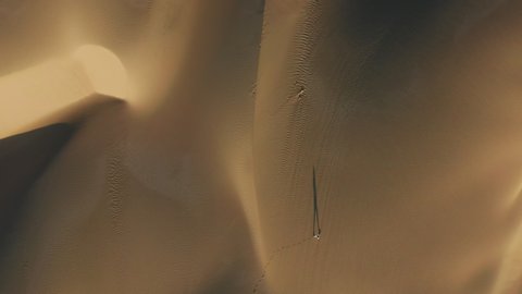 Tourist is walking through the desert natural landscape. 4K Aerial top-down drone footage of a traveler making footprints on the sandhill at sunrise. Long shadows are on golden sand, California, USA