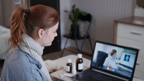 young woman with poor health communicates with female doctor online via web camera on laptop using modern technologies, while sitting at home on bed during quarantine and pandemic for coronavirus