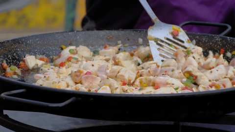 Super slow motion: chef cooking fried chicken meat pieces, peppers, peas in huge wok at summer food market - close up view. Outdoor cooking, cookery, gastronomy and street food concept