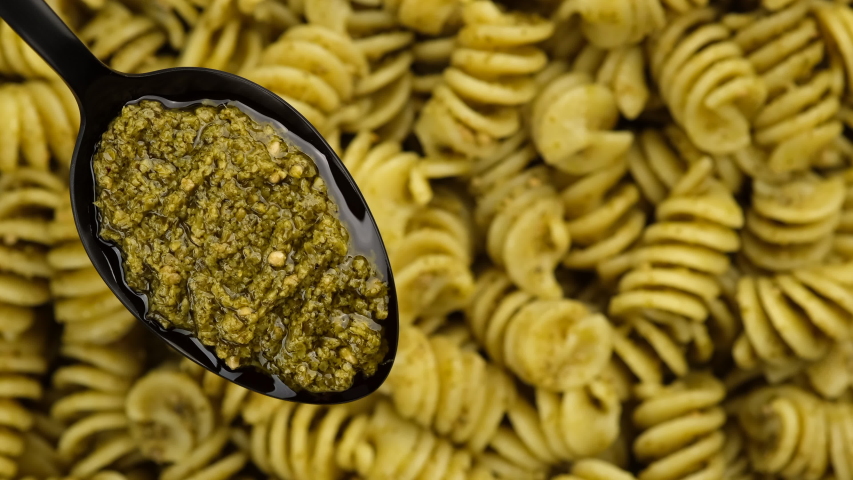 pesto alla genovese in spoon and pasta with pesto on background rotating