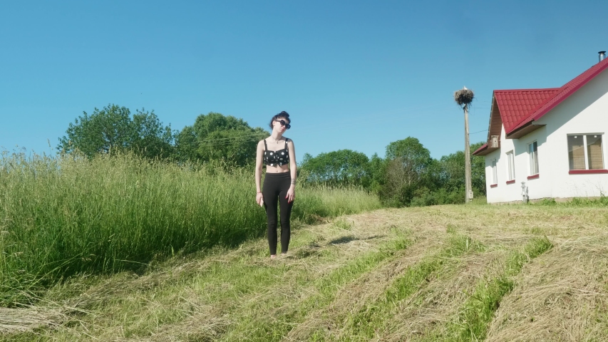 View of young pretty brunnette doing ballet in green fields on sunny summer day.