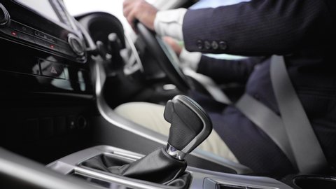 Business man in suit hand control the stick shift transmission in luxury car. Male hand changing gear driving car. 4k resolution shot.