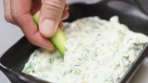 Slice of fresh cucumber is dipping into green onion dip, slow motion.