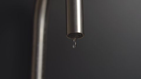 Dripping steel faucet on a black background at home