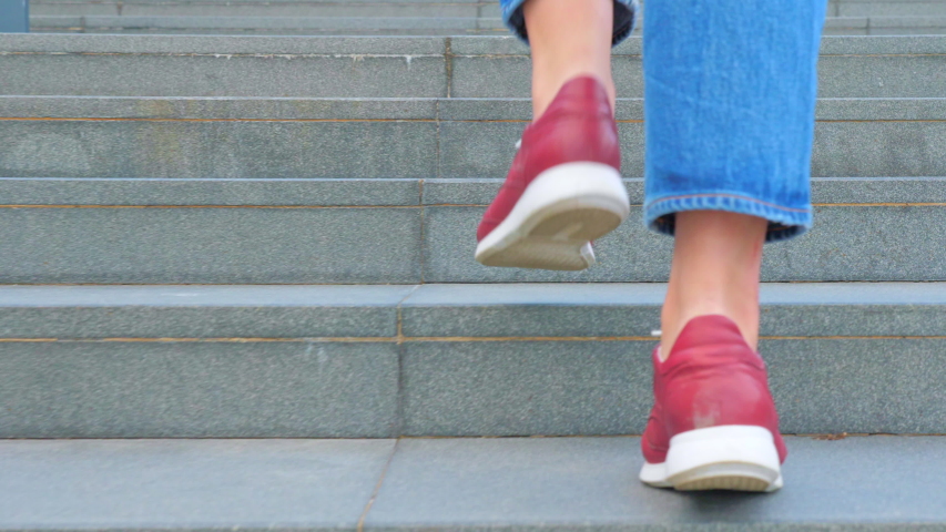 A teenage girl in red shoes and jeans climbs the concrete steps of the stairs. Close view of the legs Royalty-Free Stock Footage #1055268113