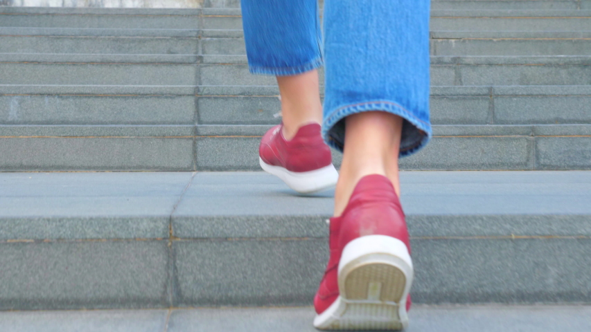 A teenage girl in red shoes and jeans climbs the concrete steps of the stairs. Close view of the legs | Shutterstock HD Video #1055268113