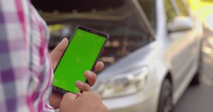 man standing near broken car searching for repair service on smartphone with green screen to VFX. Car accident. Car trouble. Close up