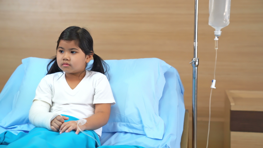 Worried mother taking care of a little girl with sick and a bone splint broken arm in hospital bed with teddy bear. Royalty-Free Stock Footage #1055276975