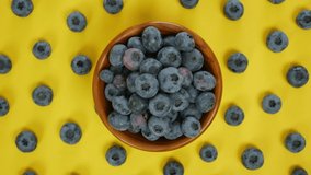 Hand places a blueberry in a bowl full of blueberries, Yellow background with scattered blueberries, 4K video