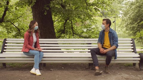 Young, happy, loving couple having date on the bench in the park During the coronavirus lockdown crisis. Relations, friendship and love concept. Social distancing and virus protection.