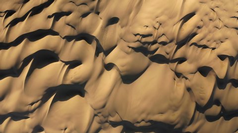 Aerial view of a drone flying over breathtaking massive golden sand dunes on sunset. 4K top-down view on the amazing wavy patterns on the desert earth. Road trip to the desert nature, California, USA