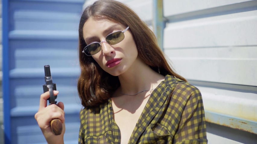 pretty mexican woman with glasses, with a revolver, aiming at the camera. pointed a gun at the camera, on the street