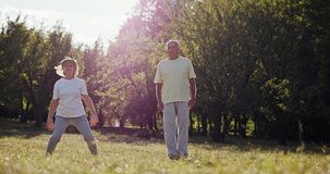 Senior retired couple exercising in a park together doing scissor bounces outdoors in the sunshine to increase mobility in a health and fitness concept