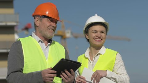 Elderly man with a tablet in his hands and a young woman at a construction site. Builders have fun discussing work issues.