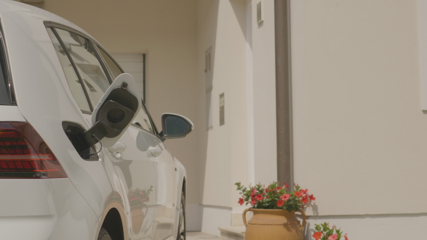 A woman walking up to her electric vehicle, plugging it in to charge in front of her house Royalty-Free Stock Footage #1055287847